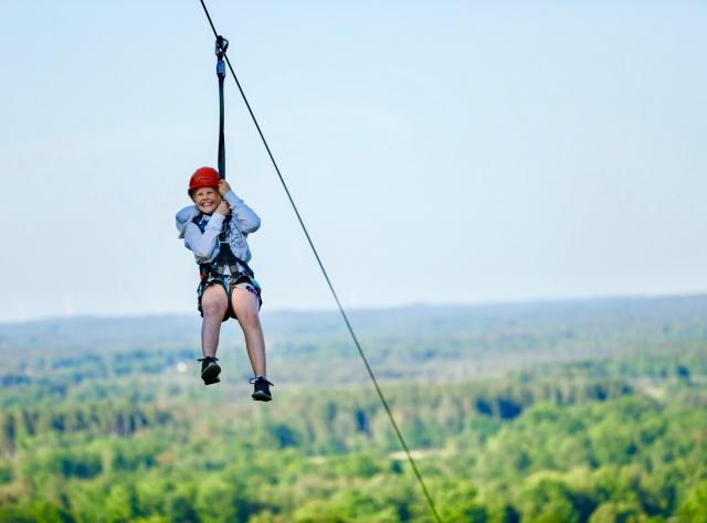 Girl rides a zipline at Kungsbygget with treetops in the background