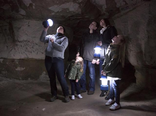 A family with lanterns admires the inside of cave at Tyckarp