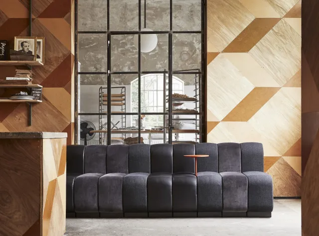 Grey sofa in middle of a wood panneled room with a floor window behind it