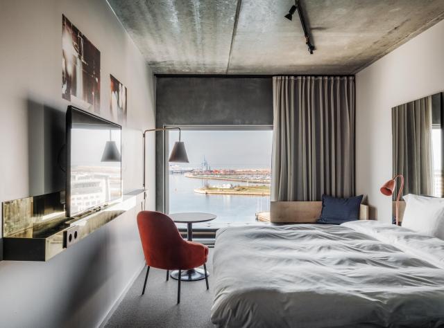 Hotellrum med säng, platt-tv, stol och stort fönster med utskik över Malmö hamn