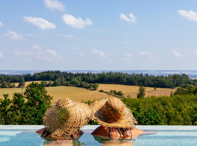 Två kvinnor med stora stråhattar tittar ut över landskapet från en pool