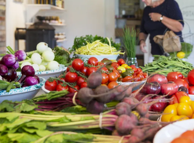 A mix of Vegetables on a table and a woman shopping in the background 