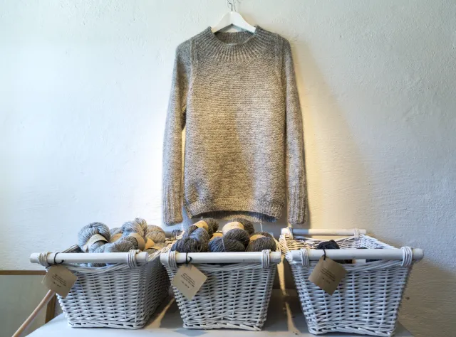 A wool sweater hanging on the wall with three baskets underneath containing yarn