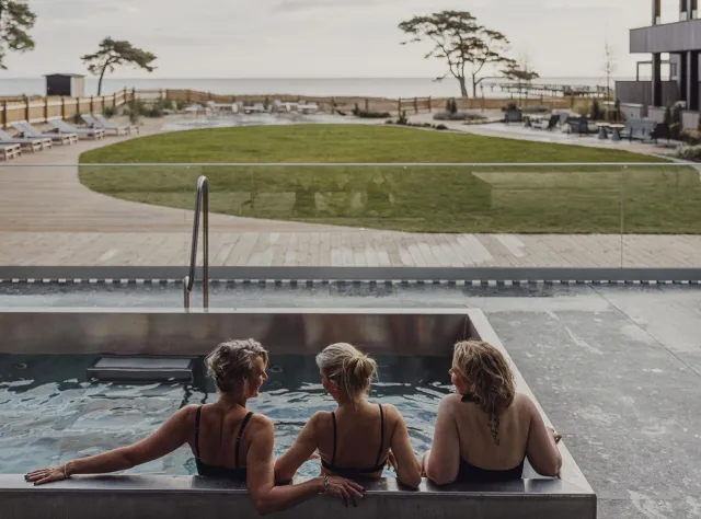Three women sit in a pool in front of a sea view