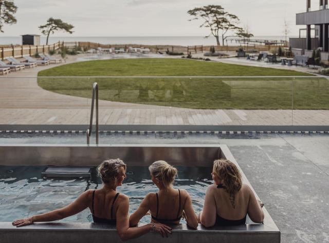 Three women sit in a pool in front of a sea view
