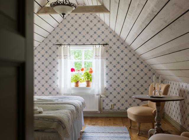 Hotel room with sloped attic ceiling and intricately patterned wallpaper creating a vintage charm