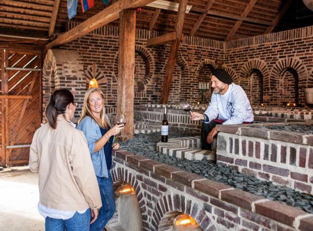 Besökare som guias i historisk tegelvinkällare med välvt tak, undersöker vinutställningar medan guide förklarar vinproduktion i Marani-källare