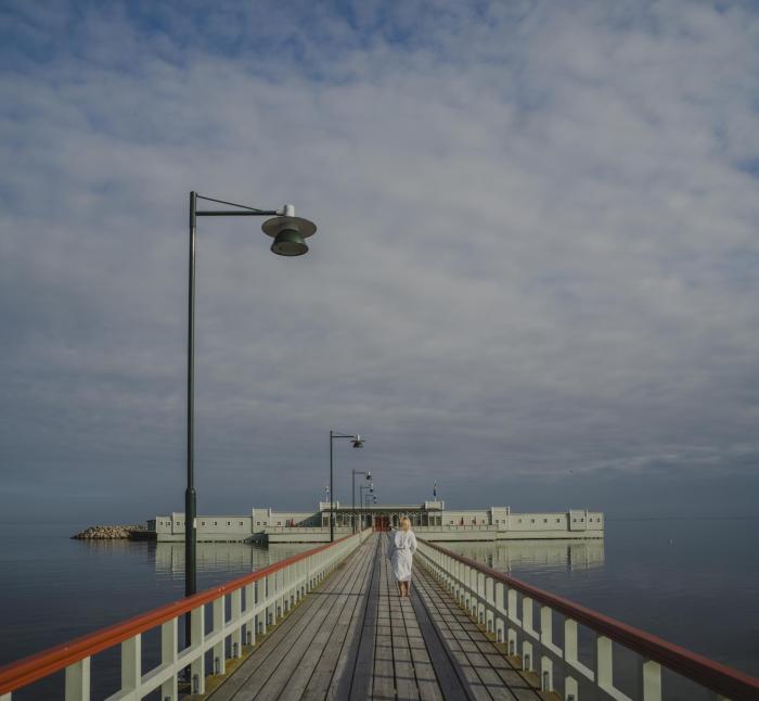 Pier with lampost leading to green open-air bathhouse surrounded by the sea