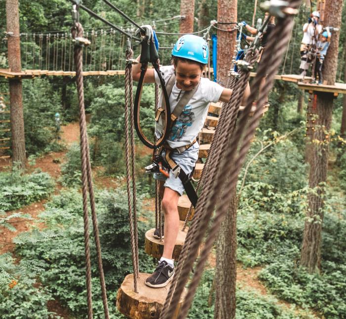 Ein Kind mit Helm klettert im Hochseilgarten Upzone durch die Baumkronen.