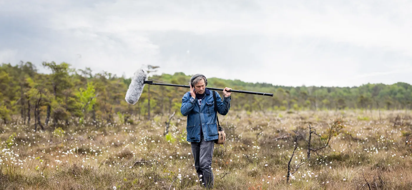 A man in a field holding a microphone.
