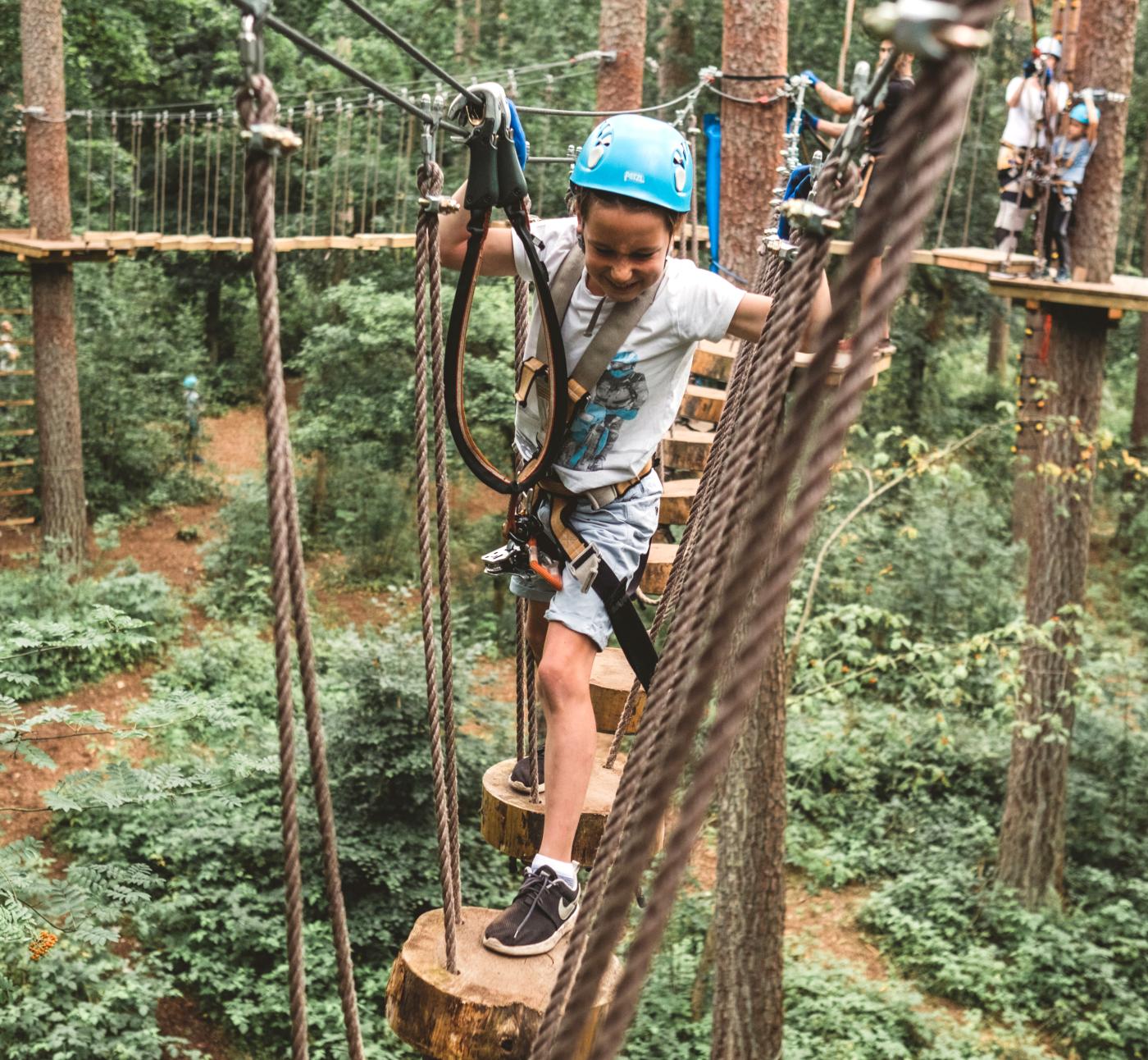 Ein Kind mit Helm klettert im Hochseilgarten Upzone durch die Baumkronen.