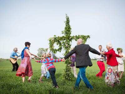 A group of people dancing and singing around the traditional midsummerpole 
