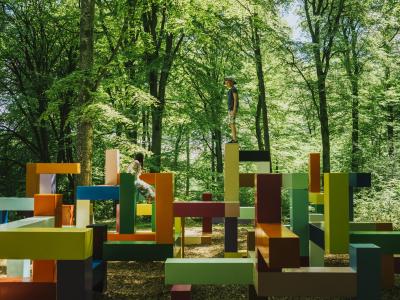Kinder spielen auf einem mit abstrakten Formen gestalteten Spielplatz in Wanås, umgeben von hohen Bäumen.