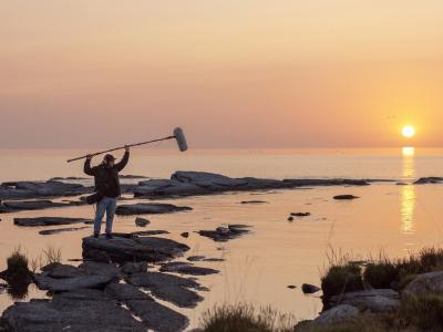 A person standing on rocks in sunrise holding a sound boom