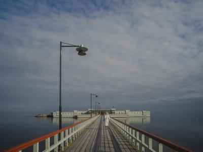 Pier with lampost leading to green open-air bathhouse surrounded by the sea
