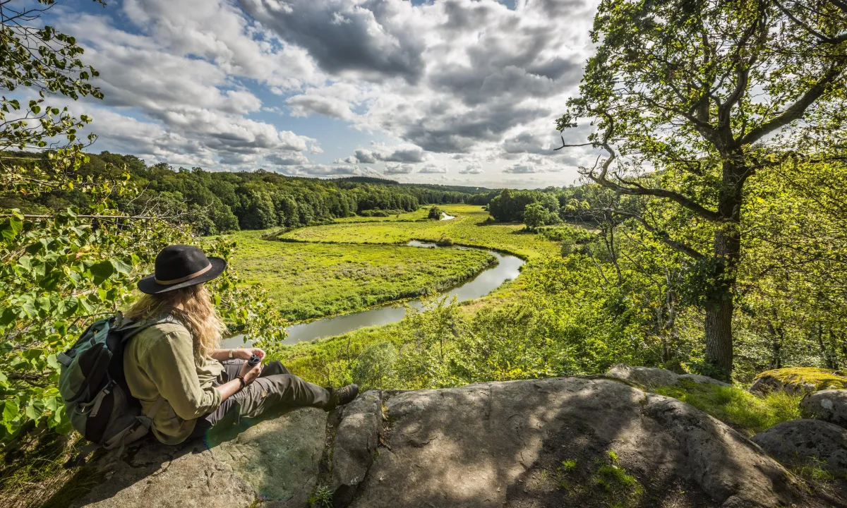 A woman siting on a Cliff overlooking a green valley